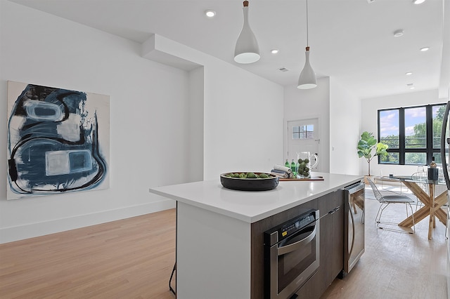 kitchen featuring wine cooler, light hardwood / wood-style floors, a kitchen island, oven, and decorative light fixtures