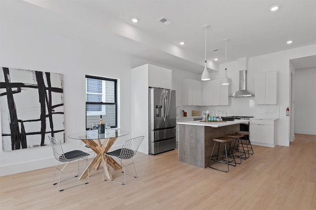 kitchen with appliances with stainless steel finishes, a breakfast bar, white cabinets, wall chimney range hood, and decorative light fixtures