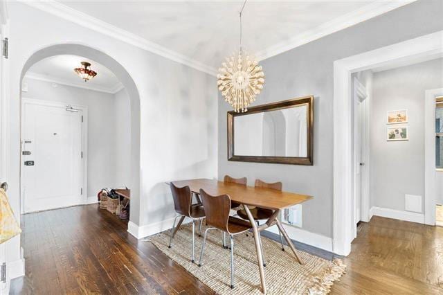 dining area with dark wood-type flooring, crown molding, and an inviting chandelier