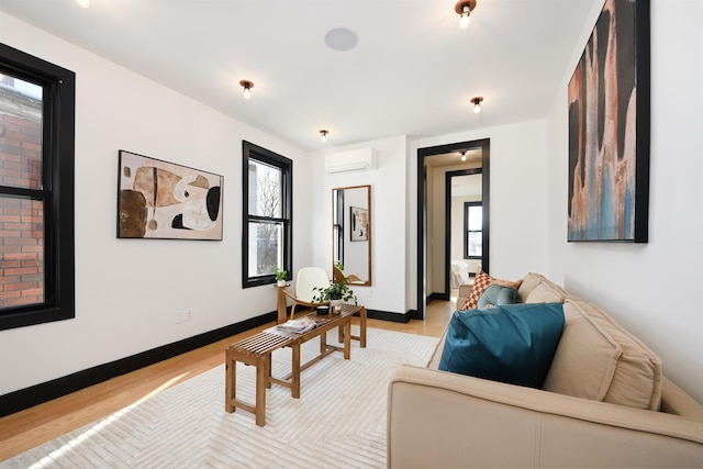 living room with baseboards, a wall mounted AC, and light wood-style floors