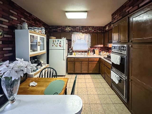 kitchen featuring light countertops, freestanding refrigerator, black oven, and brick wall