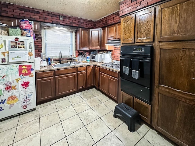kitchen with a textured ceiling, light tile patterned floors, a sink, black oven, and freestanding refrigerator