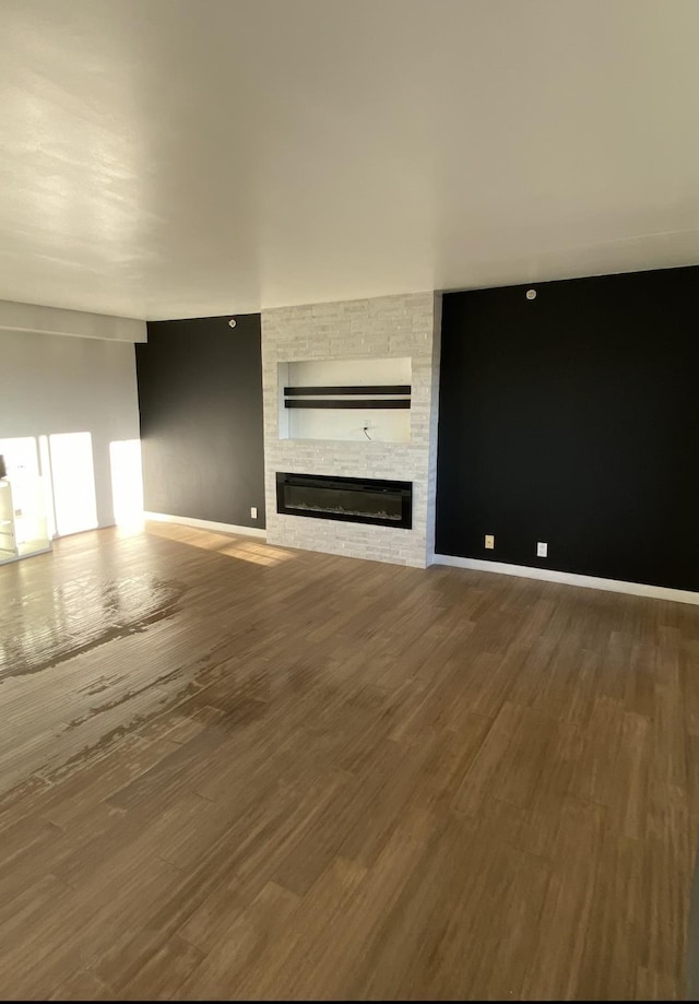 unfurnished living room featuring a stone fireplace, wood finished floors, and baseboards