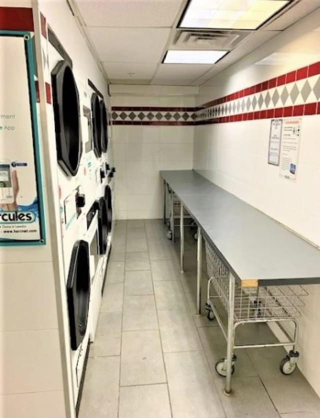 community laundry room featuring light tile patterned floors, visible vents, tile walls, and stacked washer and clothes dryer