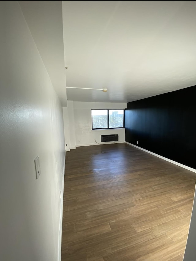 unfurnished room featuring an AC wall unit, baseboards, and wood finished floors