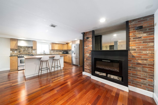 kitchen with a glass covered fireplace, visible vents, a kitchen breakfast bar, dark wood-type flooring, and stainless steel appliances