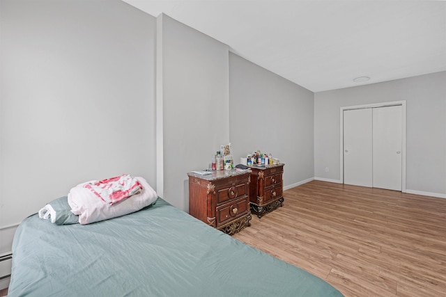 bedroom with baseboard heating, a closet, and light hardwood / wood-style flooring