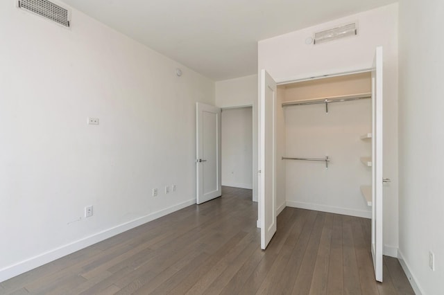 unfurnished bedroom featuring hardwood / wood-style floors, a closet, visible vents, and baseboards