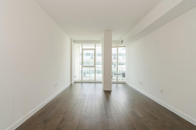 empty room with a wall of windows, dark wood-style flooring, and baseboards