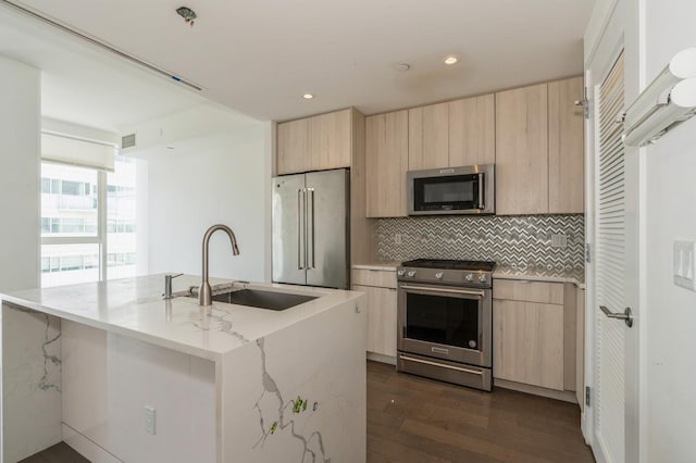 kitchen featuring high end appliances, modern cabinets, a sink, light brown cabinetry, and backsplash