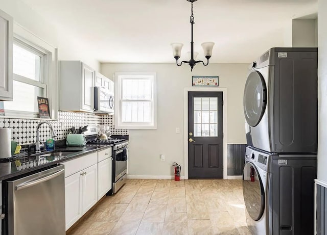 kitchen with dark countertops, backsplash, appliances with stainless steel finishes, stacked washer / dryer, and a sink