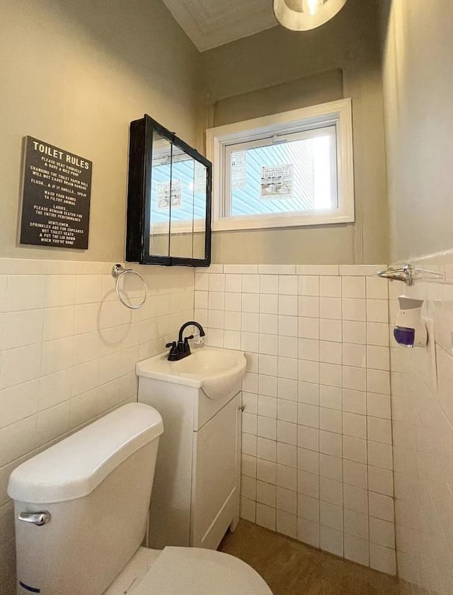 half bath with wainscoting, vanity, toilet, and tile walls