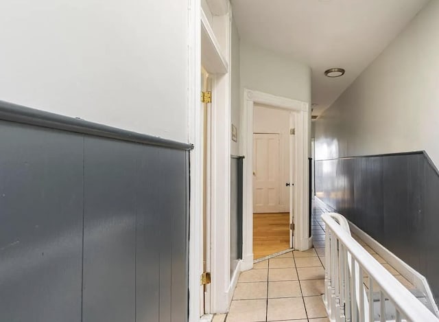 hall with light tile patterned floors, a wainscoted wall, and an upstairs landing