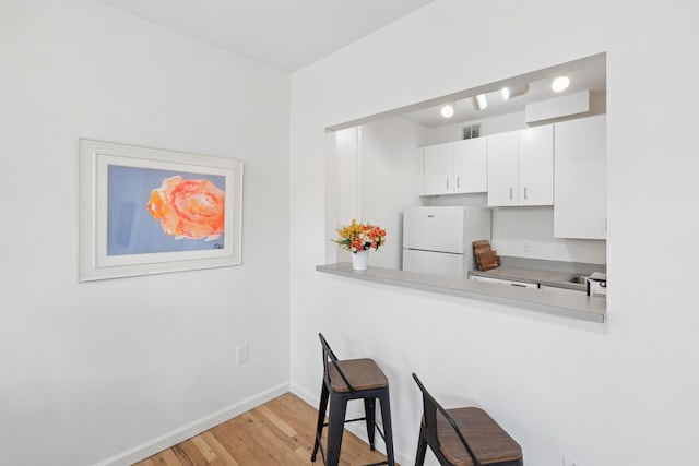 110 Morris St Unit 301, Jersey City, NJ 07302 - kitchen featuring freestanding refrigerator, light wood-type flooring, a kitchen breakfast bar, light countertops, and white cabinetry