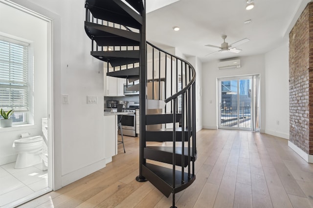 stairway with baseboards, an AC wall unit, hardwood / wood-style flooring, and a ceiling fan