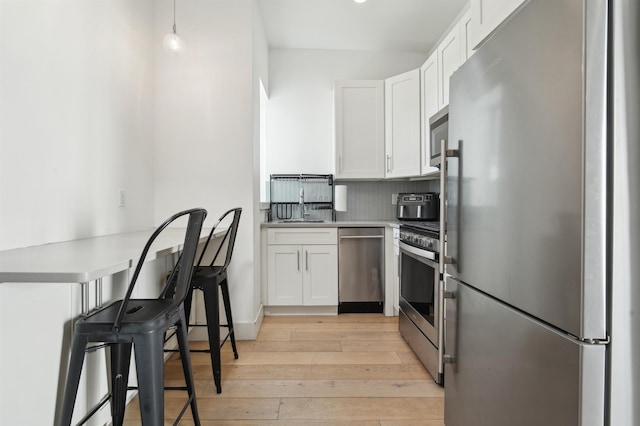 kitchen featuring light wood-style flooring, appliances with stainless steel finishes, a peninsula, white cabinetry, and backsplash