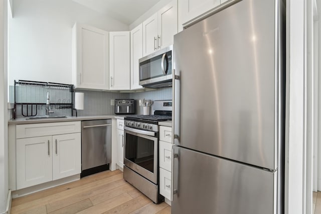 kitchen with light wood-style flooring, stainless steel appliances, a sink, white cabinets, and decorative backsplash