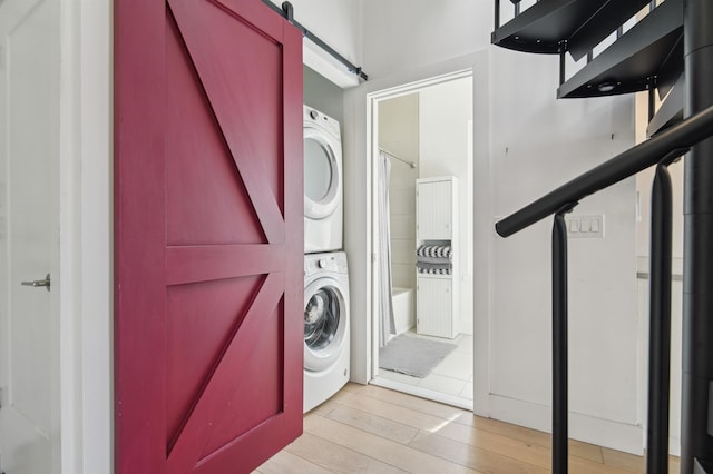 washroom with laundry area, a barn door, wood finished floors, and stacked washer / drying machine