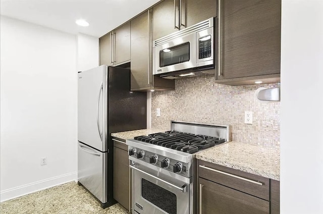 kitchen with dark brown cabinets, appliances with stainless steel finishes, light stone counters, baseboards, and decorative backsplash