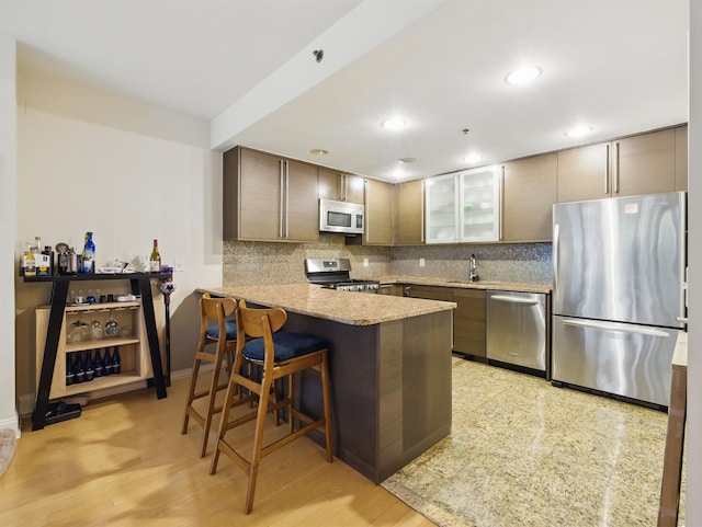 10 Regent St # 308, Jersey City, NJ 07302 - kitchen featuring stainless steel appliances, a peninsula, tasteful backsplash, a breakfast bar area, and glass insert cabinets