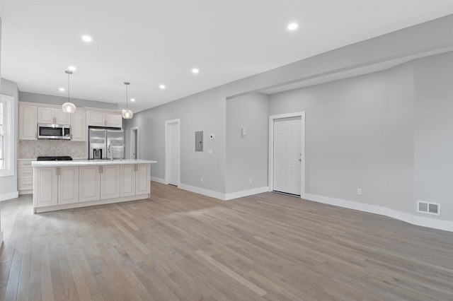 kitchen with decorative light fixtures, light wood-type flooring, a kitchen island, decorative backsplash, and stainless steel appliances