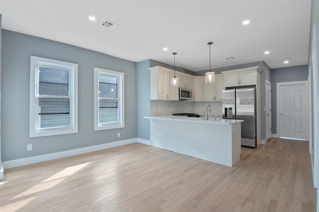 kitchen with tasteful backsplash, hanging light fixtures, light wood-type flooring, kitchen peninsula, and stainless steel appliances