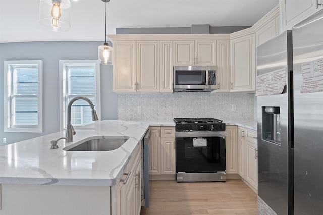 kitchen featuring appliances with stainless steel finishes, decorative light fixtures, sink, light wood-type flooring, and light stone counters