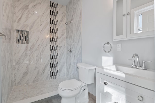 bathroom featuring tiled shower, toilet, and vanity