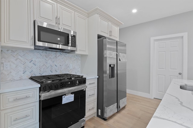 kitchen featuring appliances with stainless steel finishes, backsplash, white cabinets, light stone countertops, and light hardwood / wood-style floors