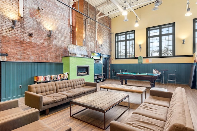 game room featuring a wainscoted wall, a glass covered fireplace, wood finished floors, and a towering ceiling