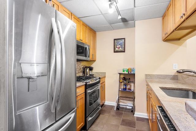 kitchen featuring appliances with stainless steel finishes, a paneled ceiling, a sink, and light stone counters