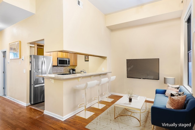 kitchen featuring a breakfast bar, stainless steel appliances, visible vents, backsplash, and wood finished floors