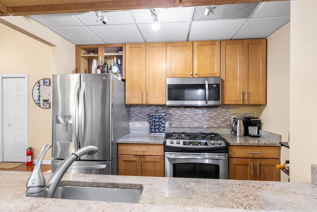 kitchen with decorative backsplash, appliances with stainless steel finishes, light stone countertops, a paneled ceiling, and a sink