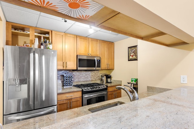 kitchen with light stone counters, tasteful backsplash, a paneled ceiling, appliances with stainless steel finishes, and a sink