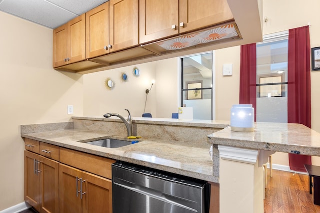 kitchen featuring kitchen peninsula, light stone countertops, stainless steel dishwasher, sink, and light hardwood / wood-style flooring