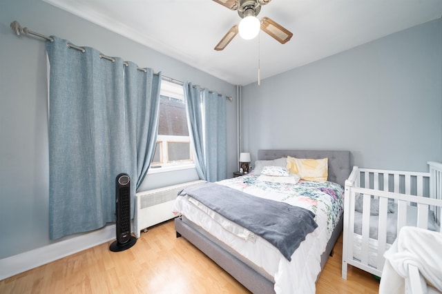 bedroom with ceiling fan, wood finished floors, and radiator