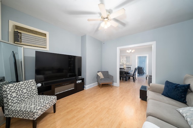 living room featuring baseboards, a wall unit AC, ceiling fan with notable chandelier, and light wood-type flooring