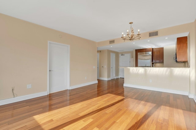 unfurnished living room with wood-type flooring, sink, and an inviting chandelier