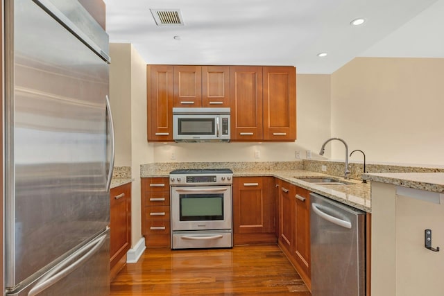 kitchen with sink, light stone counters, kitchen peninsula, stainless steel appliances, and hardwood / wood-style floors