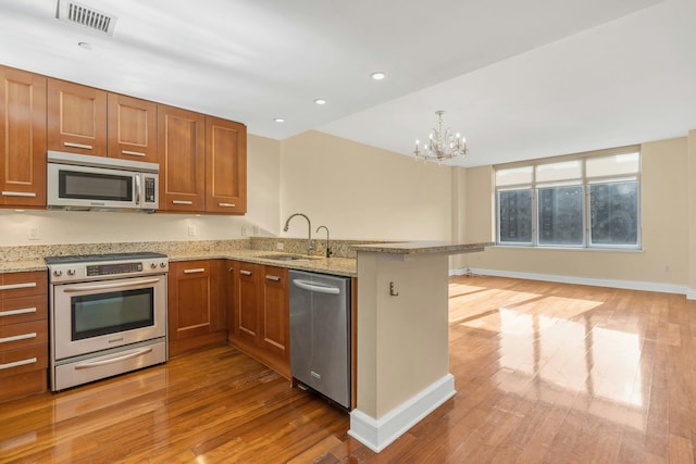 kitchen with sink, light hardwood / wood-style flooring, appliances with stainless steel finishes, light stone counters, and kitchen peninsula