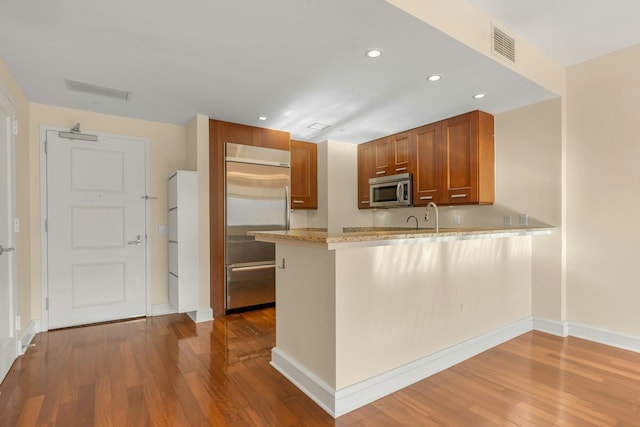 kitchen with sink, kitchen peninsula, stainless steel appliances, light stone countertops, and light hardwood / wood-style flooring