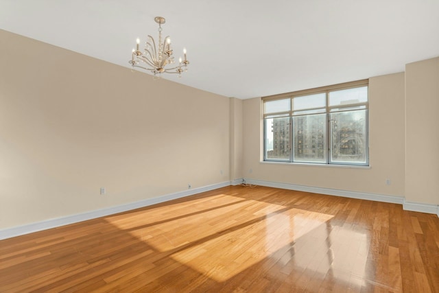 empty room featuring wood-type flooring and a notable chandelier