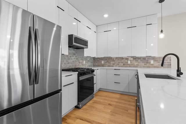 kitchen with a sink, modern cabinets, appliances with stainless steel finishes, and light wood finished floors