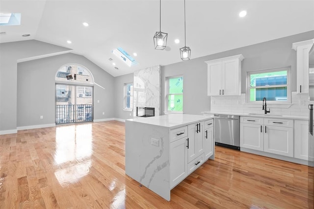 kitchen featuring dishwasher, white cabinets, a kitchen island, and vaulted ceiling with skylight