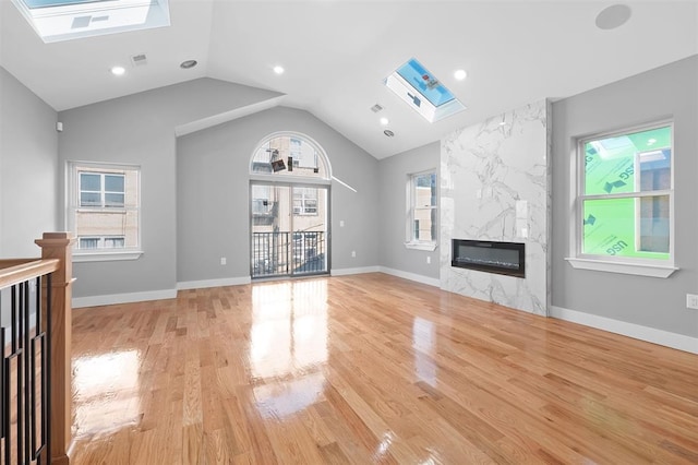 unfurnished living room featuring a premium fireplace, lofted ceiling with skylight, and light wood-type flooring