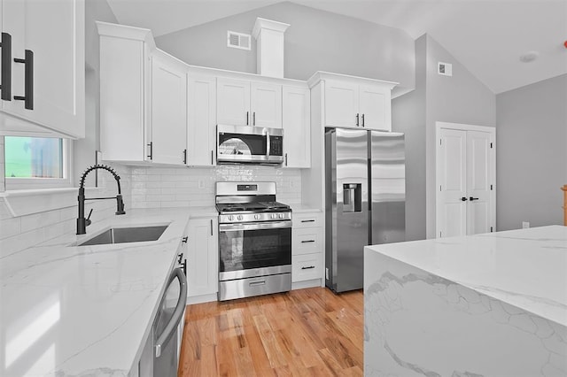 kitchen with light stone counters, stainless steel appliances, sink, light hardwood / wood-style flooring, and white cabinets