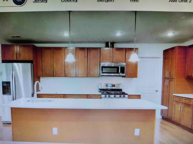 kitchen with an island with sink, decorative light fixtures, a sink, appliances with stainless steel finishes, and light countertops