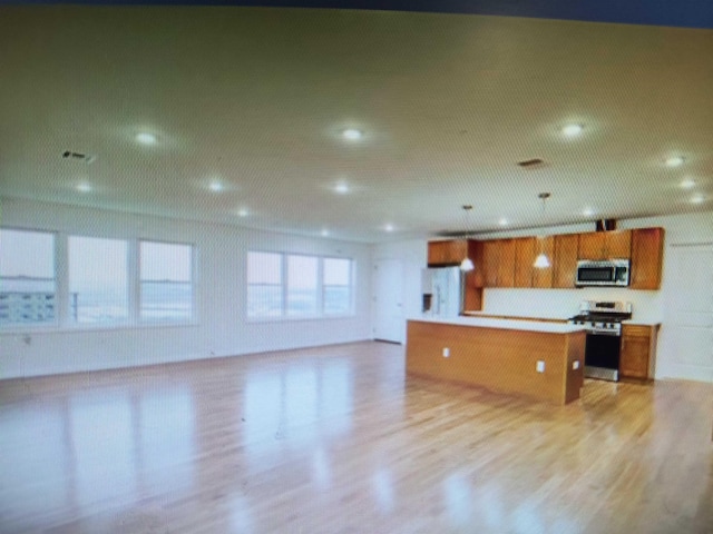 kitchen featuring brown cabinets, open floor plan, light wood-style floors, appliances with stainless steel finishes, and light countertops