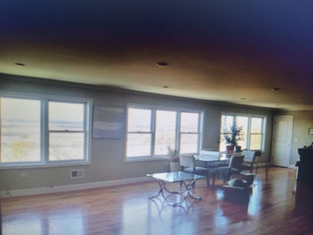 living area featuring a wealth of natural light, visible vents, baseboards, and wood finished floors