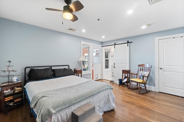 bedroom with a barn door, ceiling fan, and light wood-type flooring